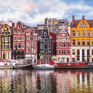 Pembe ve mavi tonlu gökyüzü altında Amsterdam kanalına sıralanmış tarihi renkli evleri, kıyıda bağlı tekneleri ve sudaki net yansımaları gösteren yüksek çözünürlüklü şehir duvar kağıdı görseli.