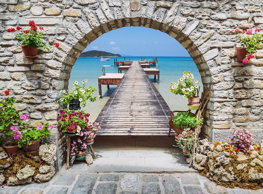 Renkli saksı çiçekleriyle bezenmiş otantik taş kemer içinden berrak turkuaz denize, adaya ve ahşap iskeleye uzanan 3D derinlik etkili sahil duvar kağıdı görseli.