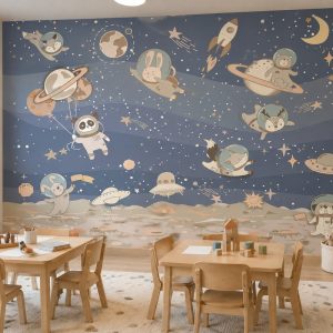 Lacivert ve mavi tonlarında uzay boşluğu ve astronot sevimli karakterler desenli duvar kağıdı önünde konumlandırılmış ahşap çocuk aktivite masaları, sandalyeler ve aydınlık zeminli sınıf ortamı.