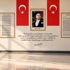 Krem/ekru zemin üzerinde ortada çerçeveli Atatürk portresi, iki yanında dikey Türk bayrakları, sol tarafta İstiklal Marşı, sağ tarafta Gençliğe Hitabe panoları ve altta "Çalışmadan, yorulmadan, üretmeden..." sözünün yer aldığı, yansıyan mermer zeminli fuaye duvar kağıdı uygulaması.