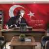 Makam odasında ahşap çalışma masası ve deri koltukların arkasında yer alan, dalgalanan Türk bayrağı ve yazı yazan Atatürk portreli "Vatanını en çok seven, görevini en iyi yapandır" sözü detaylı duvar kağıdı tasarımı.