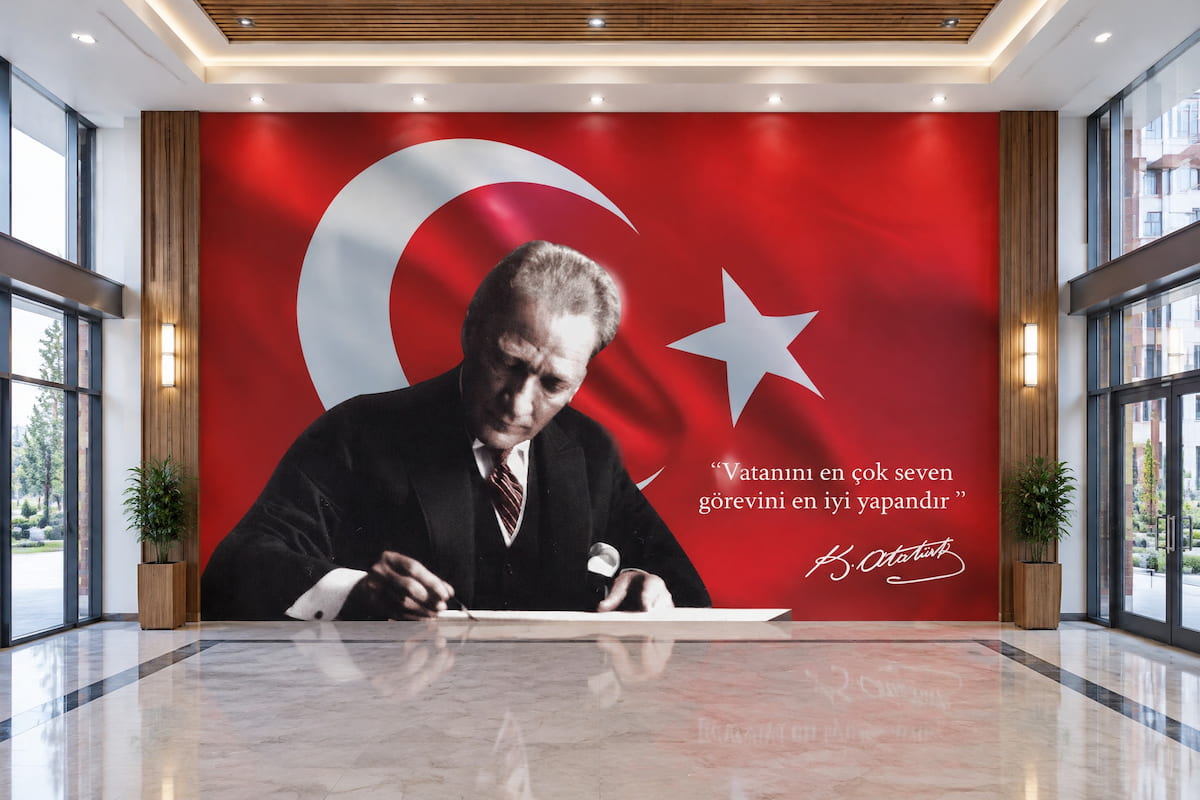 Dalgalanan kırmızı Türk bayrağı ve ay-yıldız fonunda masasında yazı yazan Mustafa Kemal Atatürk portresi ve "Vatanını en çok seven, görevini en iyi yapandır" yazılı; yansıyan mermer zeminli fuaye duvar kağıdı uygulaması.